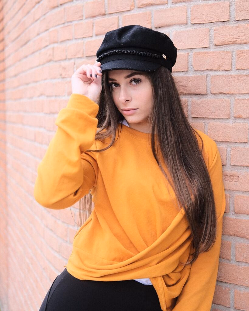 Ritratto editoriale con cappello nero davanti a una parete in mattoni